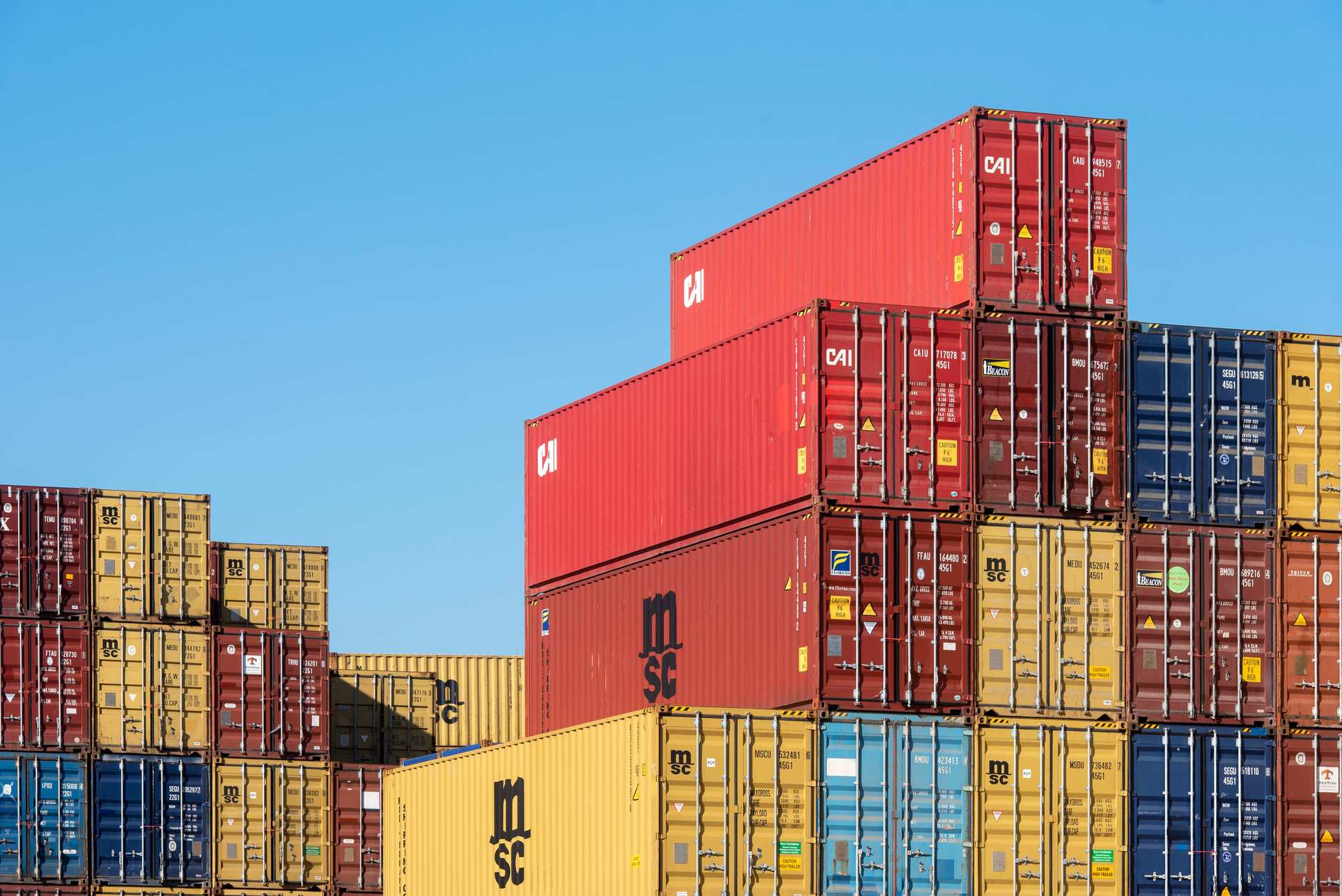 Stacked shipping containers under a clear blue sky, logistics container yard
