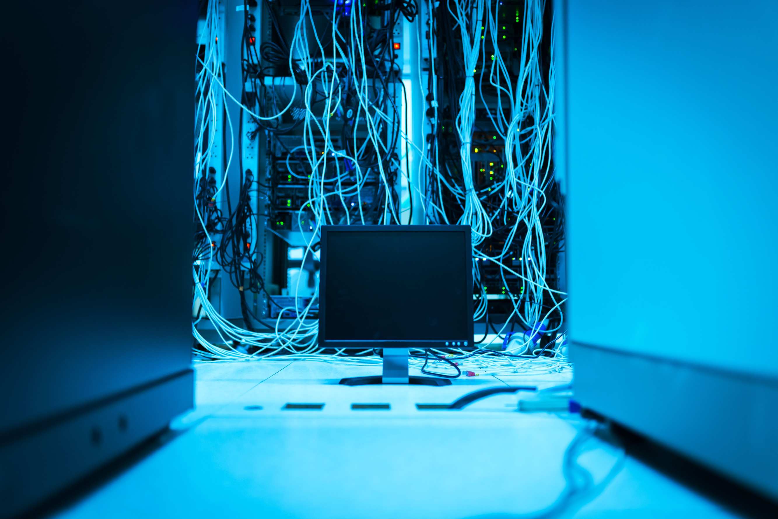 Server racks and network cabling in a data centre aisle with a monitor in the foreground